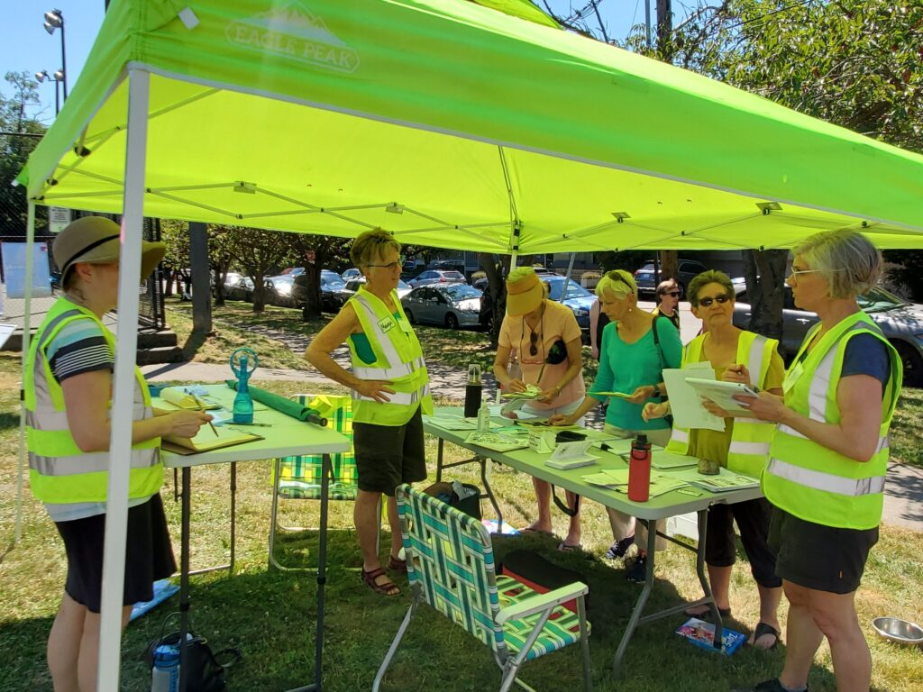 Several people gathered around tables (some wearing yellow vests), and a couple of other people--all under a yellow-canopied tent